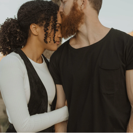 A white man kissing a black woman on the forehead