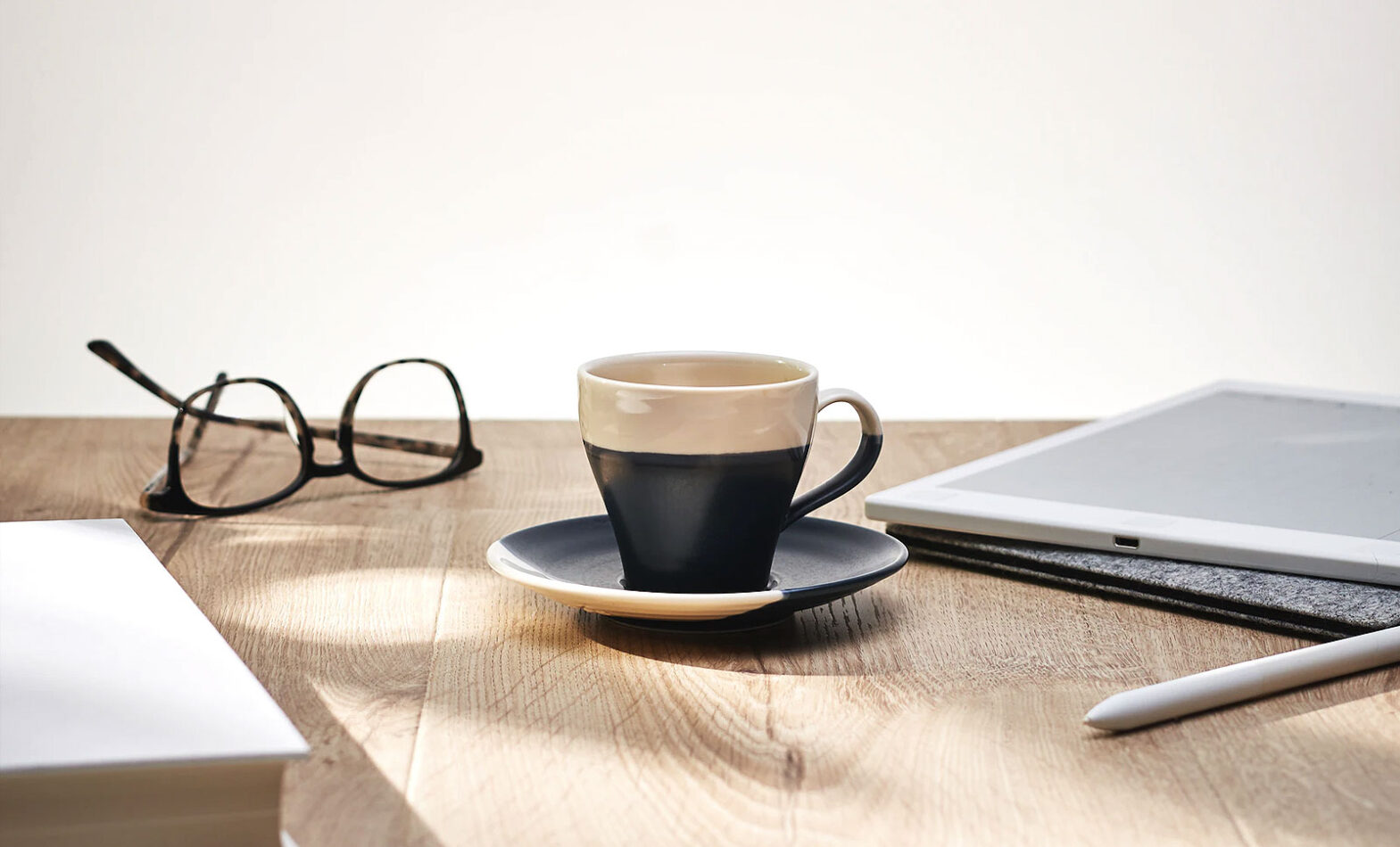 A mug and saucer next to a tablet and glasses