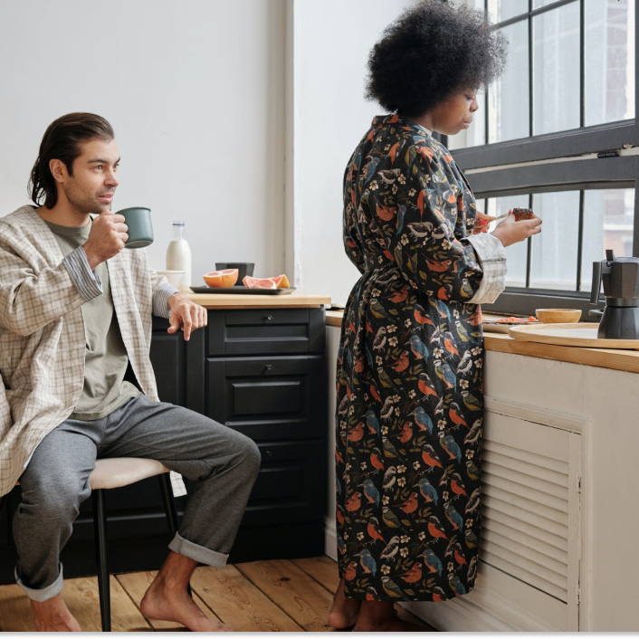 A man drinking coffee while a woman makes breakfast