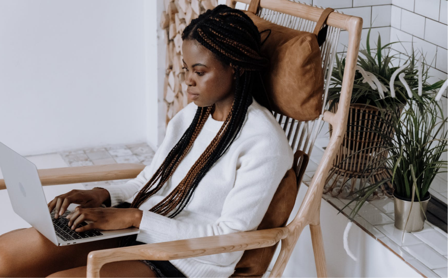 A black woman using a laptop on a wooden chair